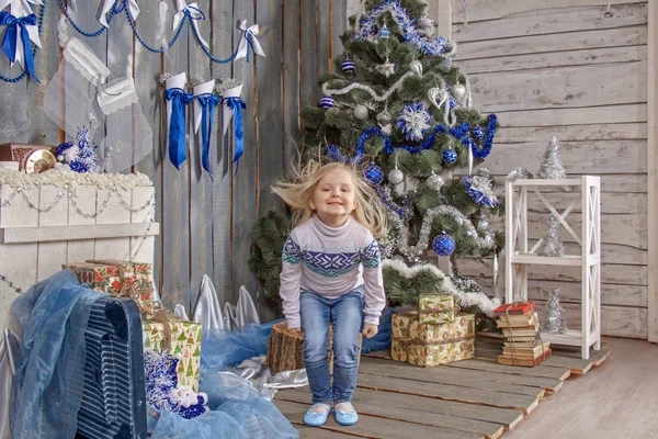 Noel süsleri takmış mavi tonlu bir kız bir Noel ağacı çalar ve süsler.