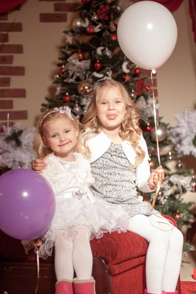 Dvě Dívky Bílými Fialovými Balónky Sedí Červeném Otomanu Vánočních Dekoracích — Stock fotografie