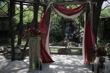 Açık hava düğün kemeri kırmızı ve beyaz kumaş ve kırmızı çiçeklerle süslenmiş.