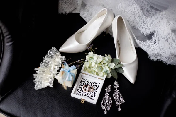 wedding accessories: wedding rings in a decorative box with flowers, earrings, women's shoes, a garter of the bride, a small gift, lace of a wedding dress