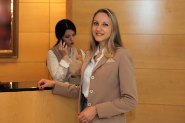 Bir yönetici konukları gülümseyerek karşılar, ikinci yönetici telefonda konuşur.