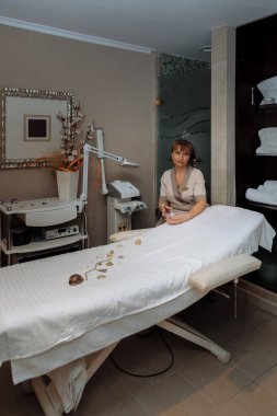 Kadın masaj terapisti masaj masasının yanına oturur ve prosedürleri uygulamaya hazırlanır.