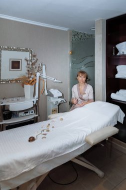 Kadın masaj terapisti masaj masasının yanına oturur ve prosedürleri uygulamaya hazırlanır.