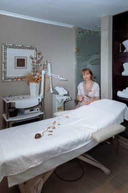 Kadın masaj terapisti masaj masasının yanına oturur ve prosedürleri uygulamaya hazırlanır.