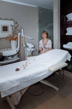 Kadın masaj terapisti masaj masasının yanına oturur ve prosedürleri uygulamaya hazırlanır.