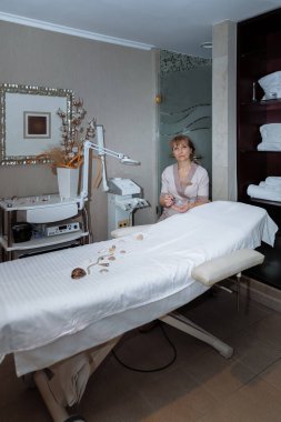 Kadın masaj terapisti masaj masasının yanına oturur ve prosedürleri uygulamaya hazırlanır.