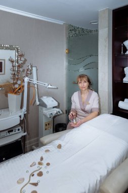 Kadın masaj terapisti masaj masasının yanına oturur ve prosedürleri uygulamaya hazırlanır.