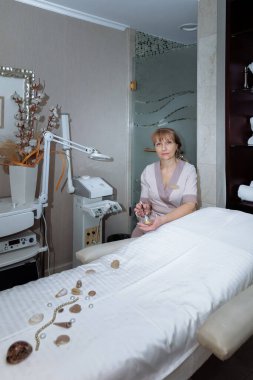 Kadın masaj terapisti masaj masasının yanına oturur ve prosedürleri uygulamaya hazırlanır.