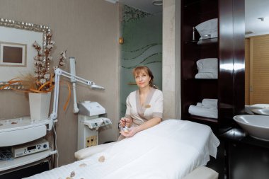 Kadın masaj terapisti masaj masasının yanına oturur ve prosedürleri uygulamaya hazırlanır.