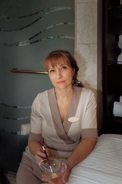 Kadın masaj terapisti masaj masasının yanına oturur ve prosedürleri uygulamaya hazırlanır.