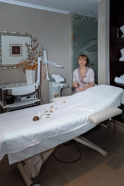 Kadın masaj terapisti masaj masasının yanına oturur ve prosedürleri uygulamaya hazırlanır.