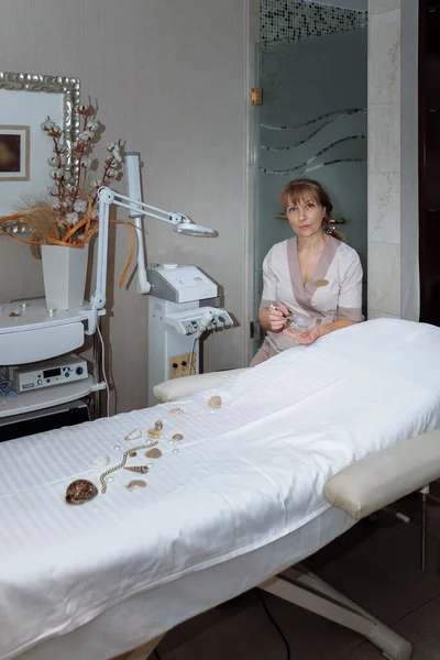 Kadın masaj terapisti masaj masasının yanına oturur ve prosedürleri uygulamaya hazırlanır.