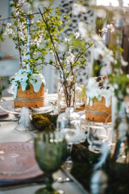 Paskalya için süslenmiş masa: Paskalya pastaları, Paskalya yumurtaları, Paskalya tavşanları, cam bardak, tabak ve bardaklarda çiçek açan kiraz dalları.