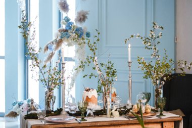 Paskalya için süslenmiş masa: Paskalya pastaları, Paskalya yumurtaları, Paskalya tavşanları, cam bardak, tabak ve bardaklarda çiçek açan kiraz dalları.