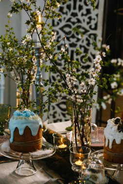 Paskalya pastaları, çiçek açan kiraz dalları, yanan mumlar, yeşil cam bardaklar.