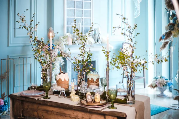 Paskalya için süslenmiş masa: Paskalya pastaları, Paskalya yumurtaları, Paskalya tavşanları, cam bardak, tabak ve bardaklarda çiçek açan kiraz dalları.