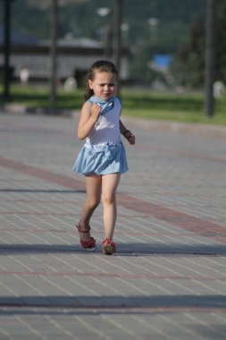Mavi ve beyaz elbiseli kız kaldırım taşlarında koşuyor.