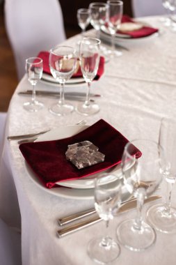 Şölen masasına yerleştirilen kırmızı peçete tabakların kenarlarına bir taş, çatal bıçak ve bardak ile bastırılır.