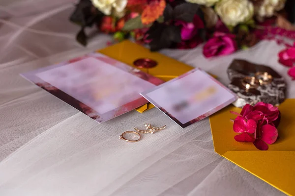 wedding accessories: a brides bouquet of roses, peonies and hydrangeas, wedding rings on a stone, a ring and earrings with diamonds, women's shoes, invitation and yellow envelopes with a red wax seal