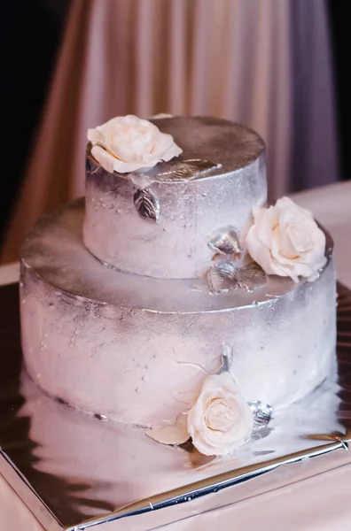 two-tier cake decorated with silver glaze and white roses