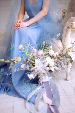 Mavi elbiseli bir kadının ayağında beyaz ortanca buketi ve pembe ranunculus.