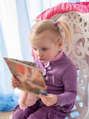 İki kuyruklu ve leylak rengi kazaklı bir kız oyulmuş bir sandalyeye oturur ve kitap okur.