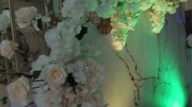 Kamera uçar, yaklaşır ve uzaklaşır duvardaki beyaz çiçeklerin çiçek aranjmanından, değişken odaklı