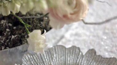 Kamera kaldırılır ve masadaki pembe ranunculus ve beyaz çan çiçeğinin çiçek aranjmanına odaklanır.