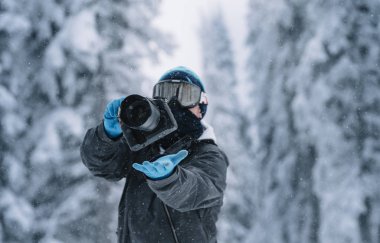 Karlı bir ormanın ortasında kamera tutan adam