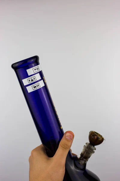 Beyaz arka planı mavi cam bong tutan izole el