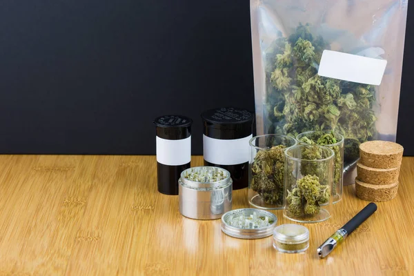 Marihuana in Containern und Plastiktüten mit Metallschleifer auf Holztisch vor schwarzem Hintergrund — Stockfoto