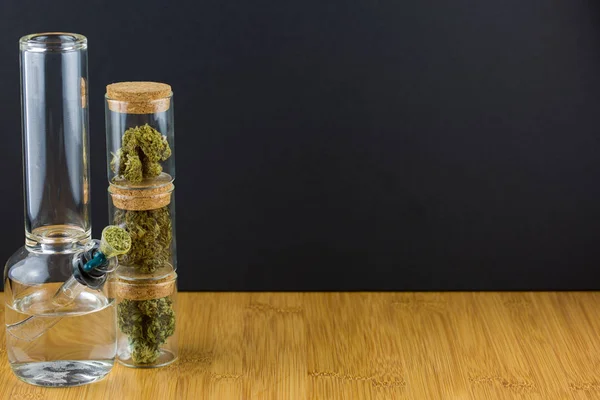 Gestapelte Glasbehälter gefüllt mit medizinischem Marihuana auf Holzoberfläche vor schwarzem Hintergrund — Stockfoto