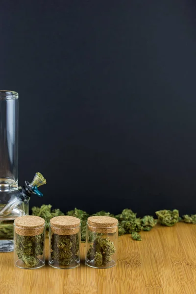 Glasgefäße gefüllt mit Marihuana in einer Reihe mit losen Knospen und einer Glasbong — Stockfoto