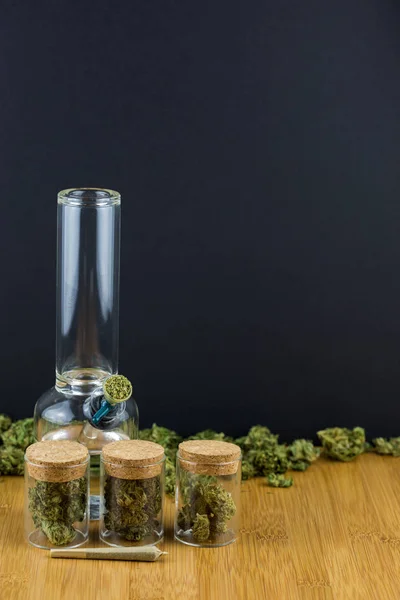 Glas gefüllt mit Marihuana in einer Reihe mit lockerer Knospe auf Holztisch vor schwarzem Hintergrund — Stockfoto