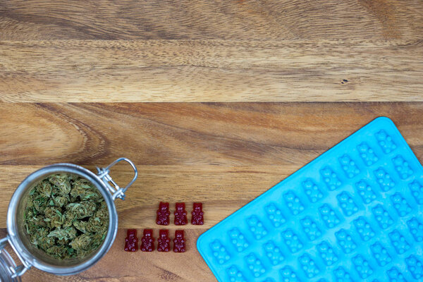 Weed buds in jar with red gummy bears with mold on wood table