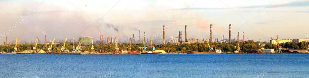 An Industrial complex, cityscape panoramic view with pipes. A river and huge buildings of metallurgical plants. Smoke emissions in the atmosphere.