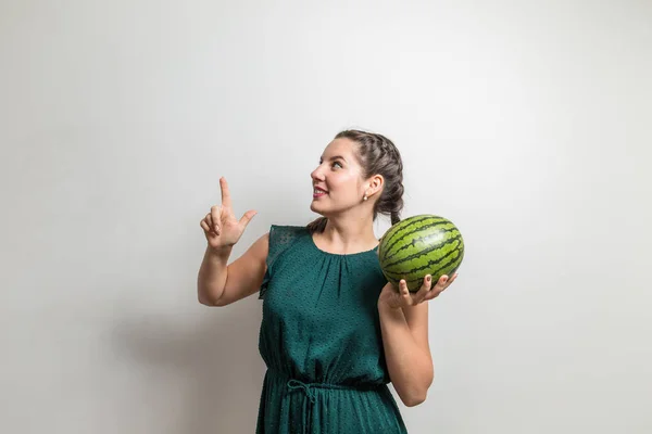 Porträtt av en leende söt flicka håller en vattenmelon och pekar finger på sida isolerade över vit bakgrund Stockfoto