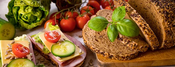 bread, fresh cereal bread with ham and vegetables, tasty healthy breakfast, top view, laid on the table, banner