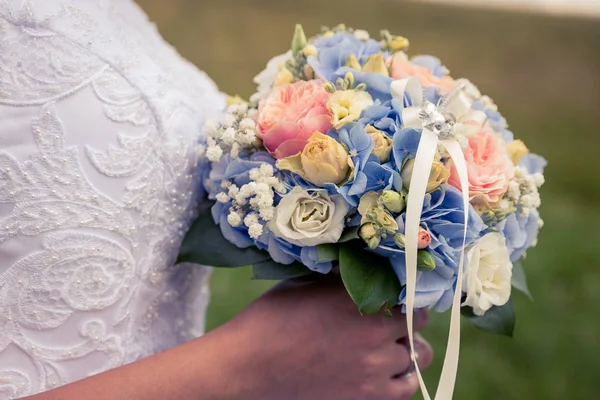 wedding bouquet, hands of bride holding a beautiful bouquet in hand, close-up of hands behind blurred background