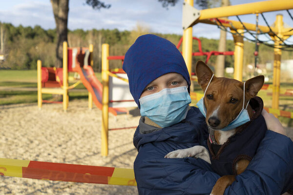 Мальчик на прогулке с собакой в парке возле закрытой игровой площадки во время карантинного КОВИД 19
