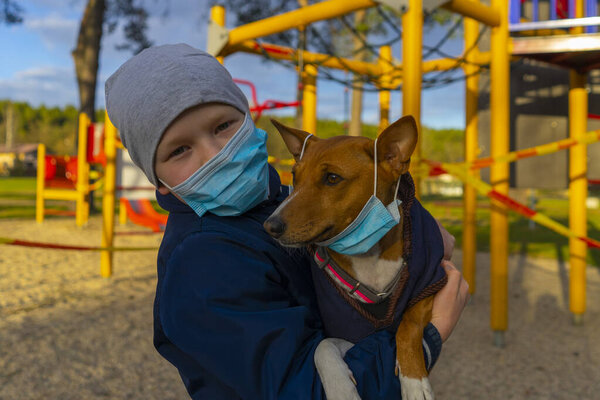 Мальчик на прогулке с собакой в парке возле закрытой игровой площадки во время карантинного КОВИД 19
