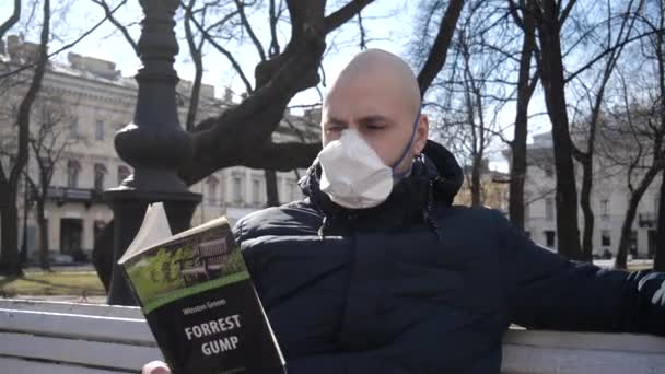 一个秃头的年轻白人感染了病毒 他坐在公园里的呼吸机里 呼吸着新鲜空气 正在看书 — 图库视频影像
