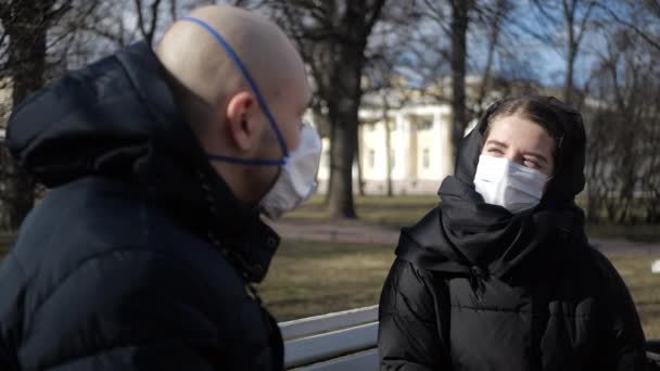隔離された患者コロナウイルスのマスクの男と女の子は距離を置かずに外に出て公園のベンチに座って — ストック動画