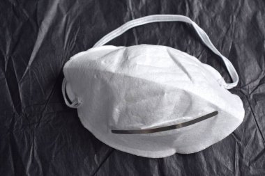 Beyaz tıbbi yüz maskesi, siyah desenli arka planda virüs koruma simgesi.