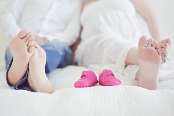 couple on bed with exposed feet baby shoes pink in front showing expecting parents maternity pregnacy
