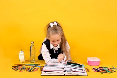 Yedi yaşında bir liseli kız, sarı arka plan, renkli kalemler, bir kalem kutusu, bir çalar saat ve bir şişe su ile açık bir kitap yığınıyla yatıyor.