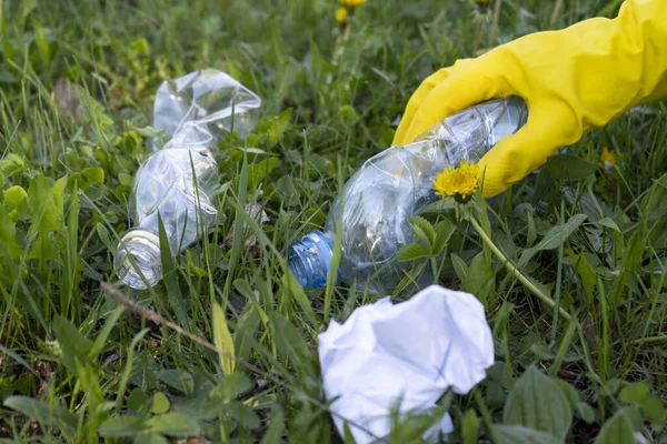 A volunteer removes garbage in the Park. A woman\'s hand in a yellow rubber glove lifts a plastic bottle