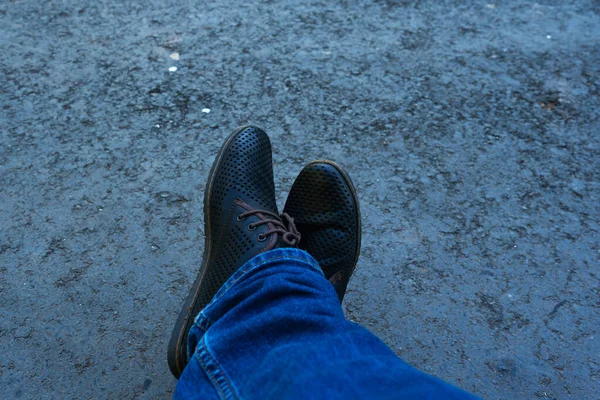 Crossed legs in jeans and shoes against the asphalt