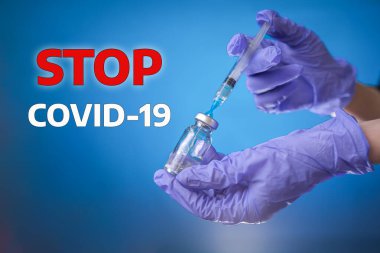 Tıbbi eldivenli bir doktor ya da bilim adamının eli bir şişe tutuyor ve şırıngayı ilaçla dolduruyor. Yazıt COVID-19 'u durdurun. Mavi arka plan. Koronavirüs, aşı ve sağlık konsepti.