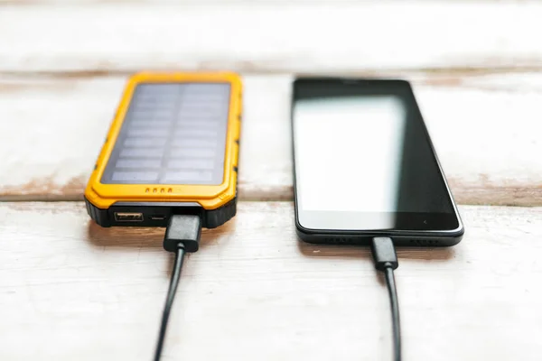Modern teknoloji ve güç bankası kavramı. Taşınabilir bir güneş şarj cihazından akıllı telefon şarj edilmiş. Yatay çizgili beyaz ahşap arka plan. Kapat..